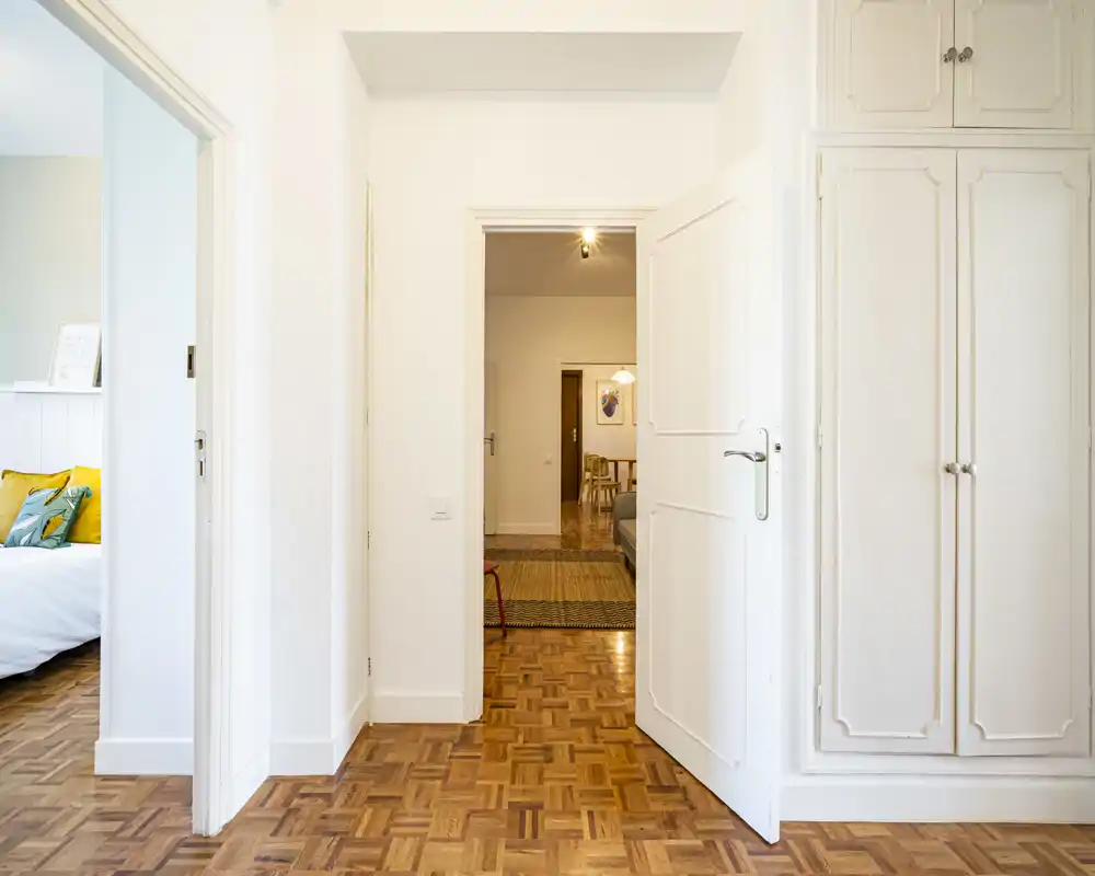 Bright, clean entrance/hallway with parquet flooring and built-in storage. The image shows a central doorway leading to adjacent rooms, ideal for listing the apartment's entry and circulation space.