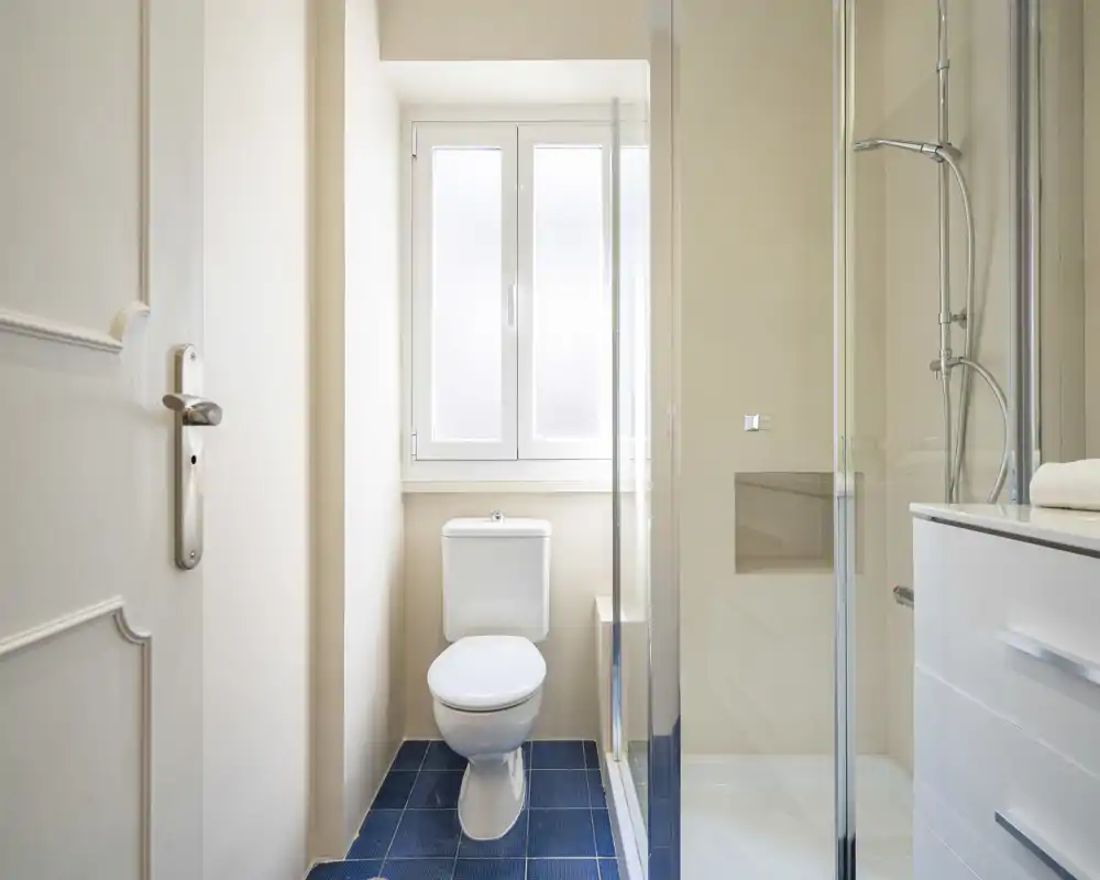 Bright, modern bathroom with a toilet, glass shower enclosure and a white vanity — clean lines and natural light from the frosted window.