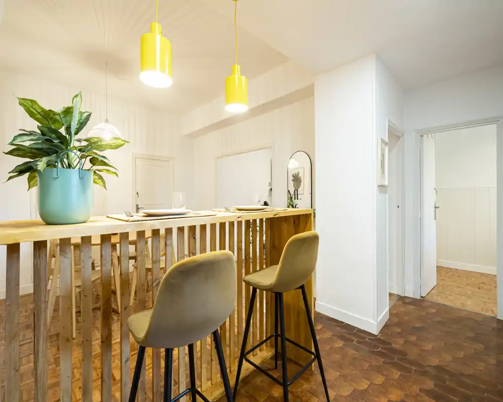 Bright open-plan dining/bar area with two upholstered bar stools, wooden slatted counter and modern pendant lights — a cozy spot for casual meals.