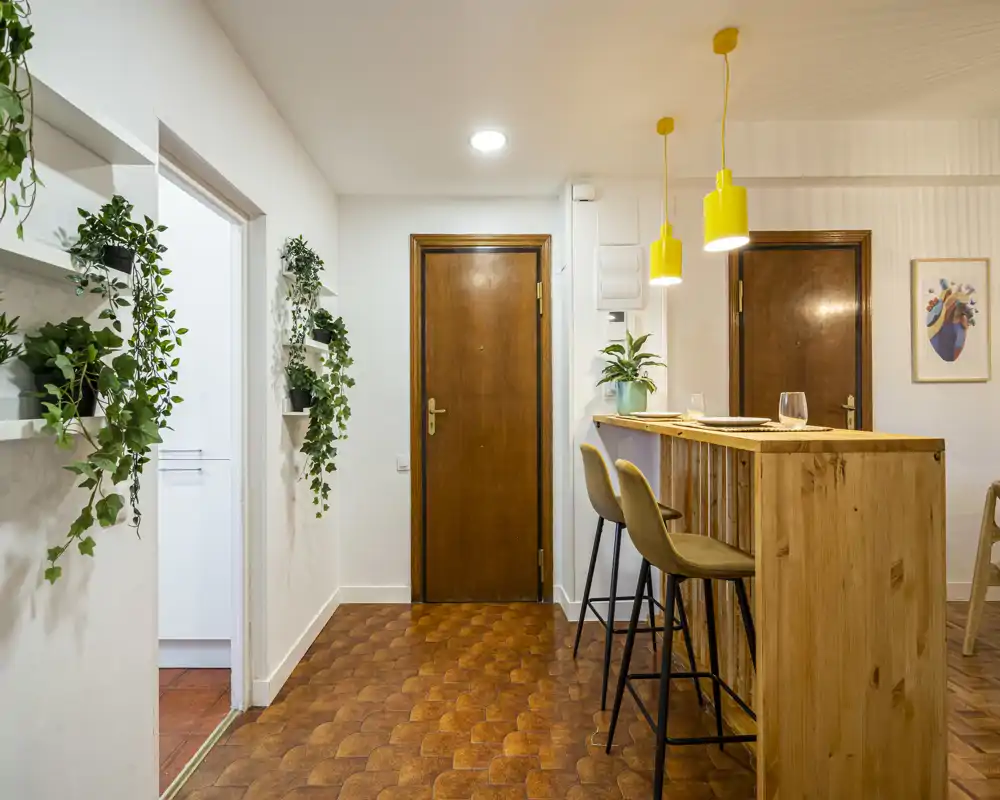 Welcoming entryway with a wooden front door, bar-style counter with stools, hanging pendant lights and green plants that add freshness.