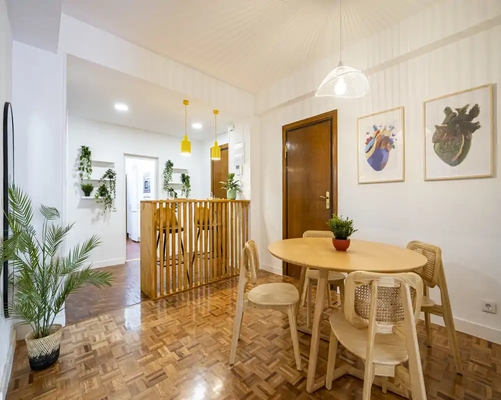 Bright, warm dining area with a round wooden table and woven chairs, pendant lighting and leafy plants creating a cozy, modern atmosphere.