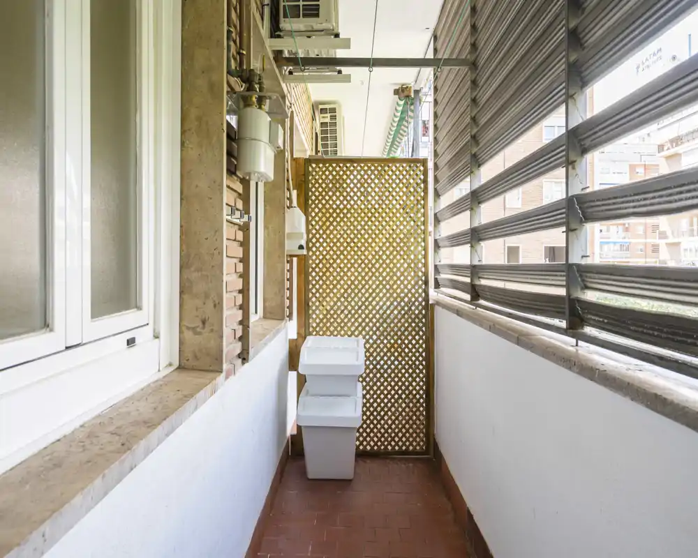 Narrow covered balcony with protective slatted shutters and tiled floor, suitable for storage or a small utility area.