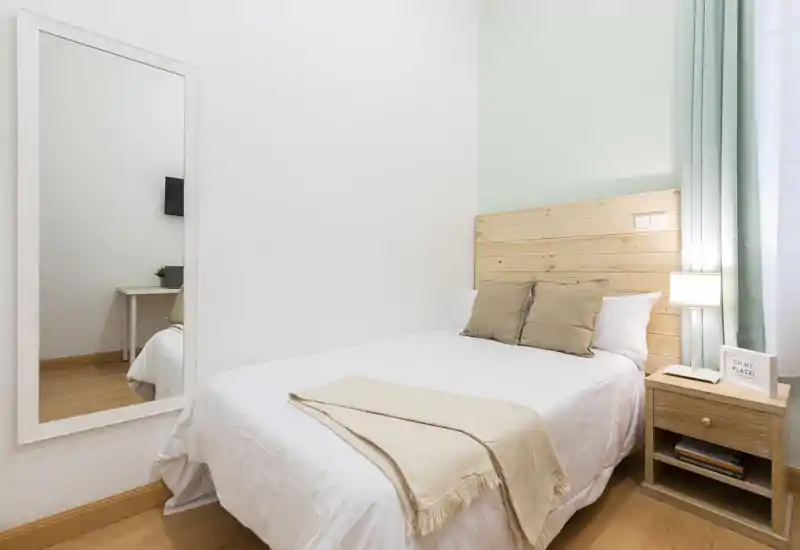 Chambre lumineuse et bien mise en scène avec tête de lit en bois, table de chevet et lampe. Textiles doux et tons neutres pour une ambiance calme et accueillante, idéale pour une annonce.