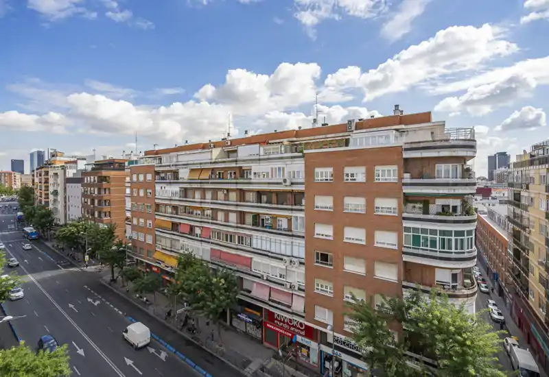 Façade d'immeuble et rue de la ville avec balcons, commerces en rez-de-chaussée et ciel dégagé — parfait pour présenter l'immeuble et son environnement urbain.