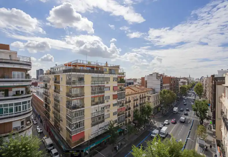 Belle vue urbaine panoramique depuis un balcon donnant sur une large avenue, des immeubles résidentiels et un ciel bleu parsemé de nuages.