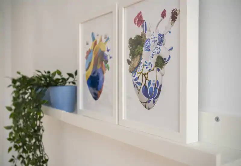 Gros plan de cadres posés sur une étagère murale avec une plante retombante ; détail décoratif plutôt qu'une vue complète de la pièce.