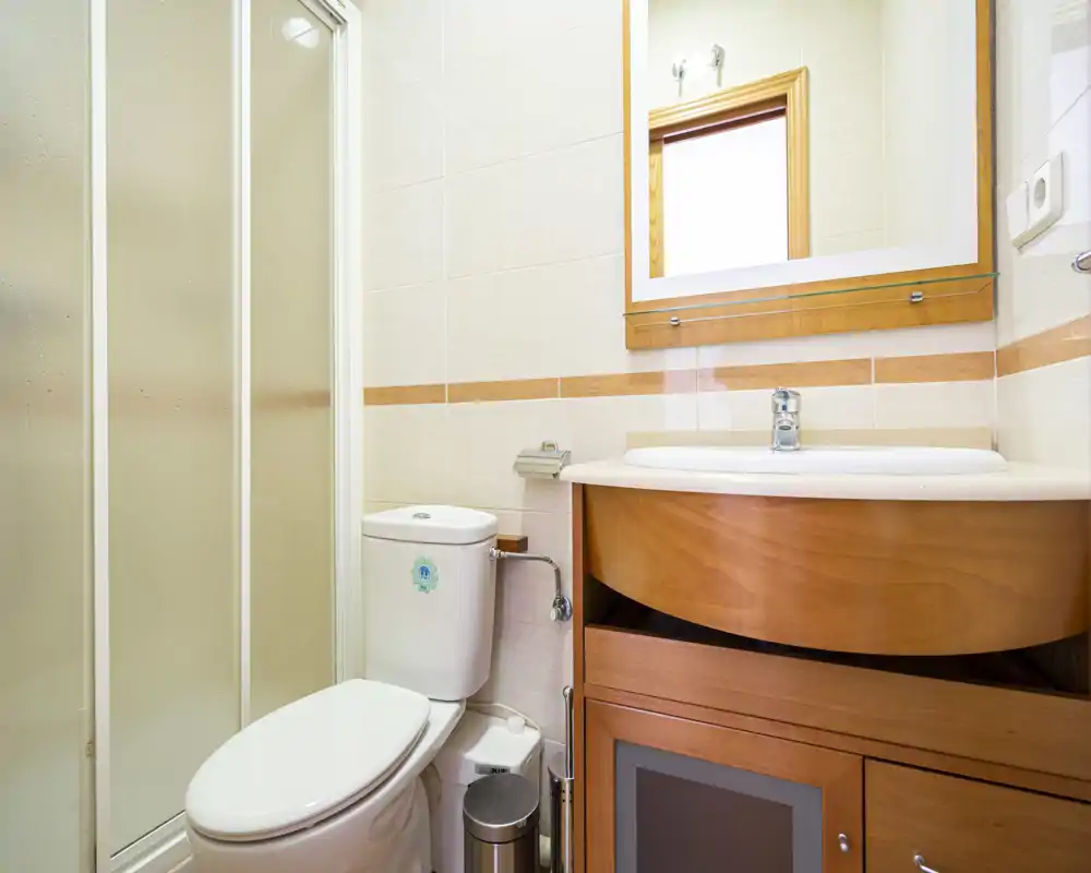 Bagno pulito e luminoso con doccia angolare, WC, mobile lavabo in legno e specchio — ideale per un bagno compatto in affitto.