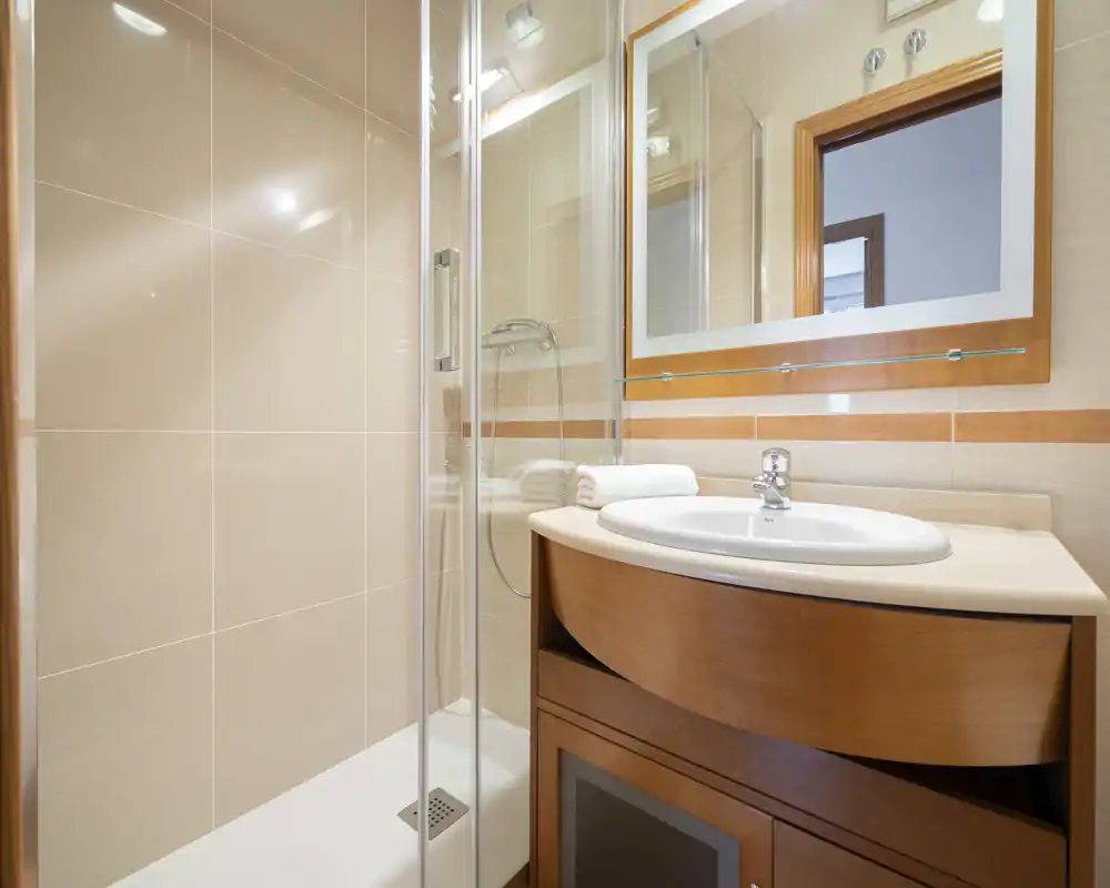 Bright, modern bathroom with a glass shower enclosure, wall-mounted mirror and a wooden vanity with integrated sink. Neutral tiles and clean lines create a fresh, well-maintained space ideal for rental listings.