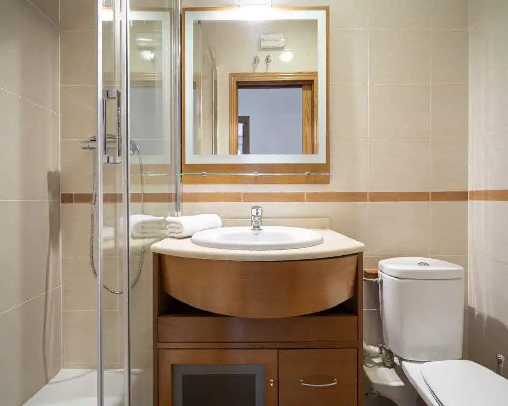 Bright, modern bathroom with a wooden vanity, round sink, glass shower and toilet — clean and well lit.