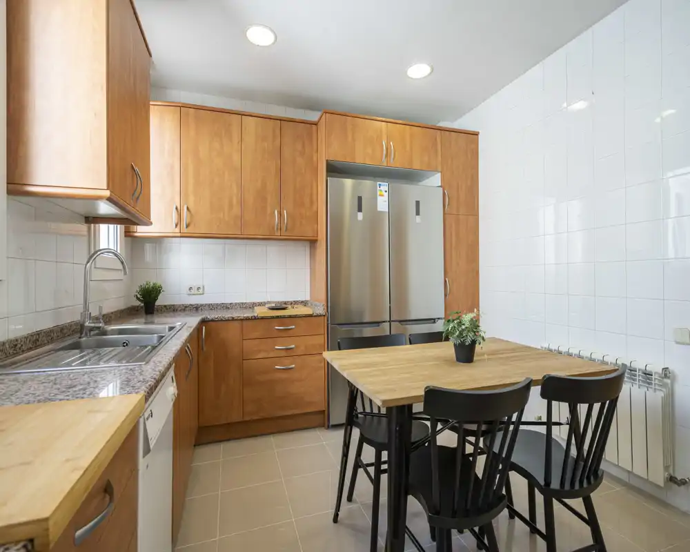 Bright, modern kitchen with wooden cabinets, stainless steel appliances and a small dining table; ideal for everyday cooking and casual meals.