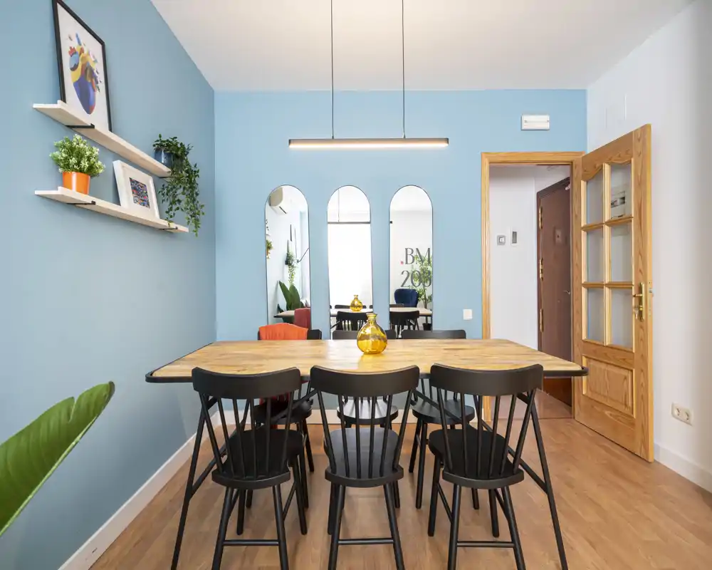 Stylish dining area with a large wooden table, six black chairs and soft blue accent walls; bright, well-styled space ideal for meals and working from the table.