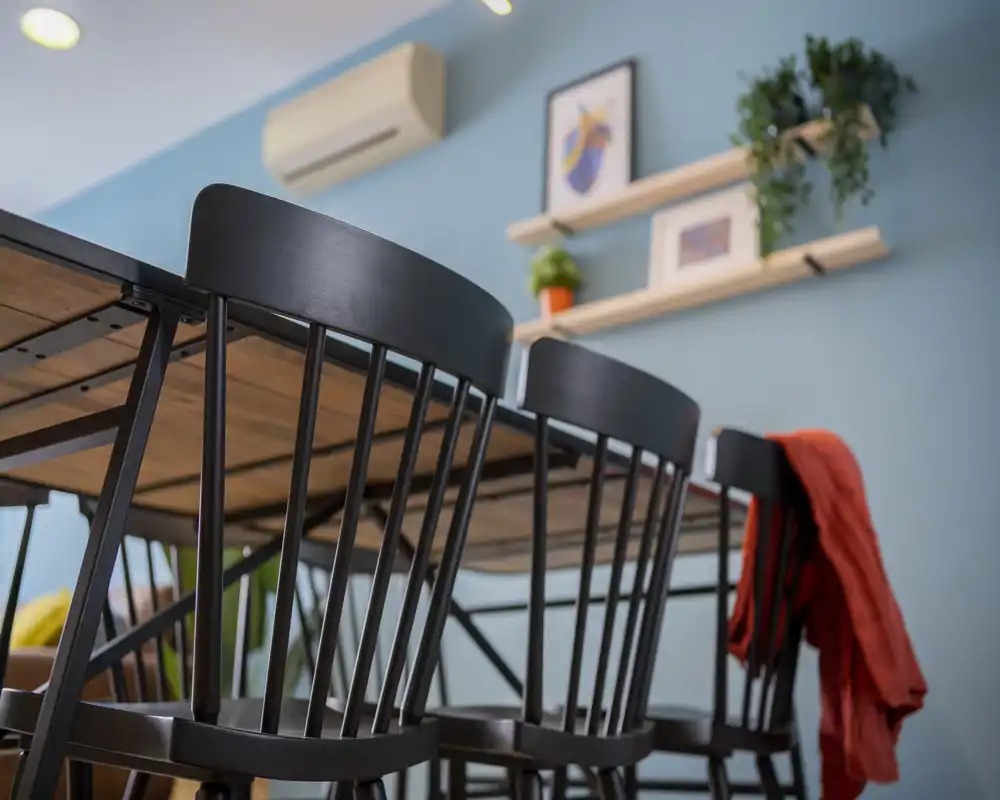 Stylish dining area with black spindle-back chairs around a wooden table, accented by wall shelves, plants and framed art; well lit and tastefully styled for a welcoming meal space.