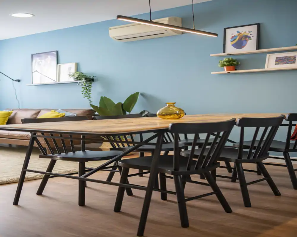 Stylish dining area with a long wooden table and black chairs, warm wood flooring and teal accent wall; bright, modern and inviting space ideal for shared meals.