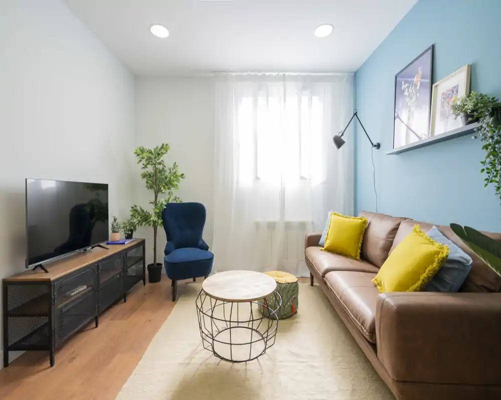 Bright, stylish living room with a leather sofa, colorful cushions, a blue accent chair and a central coffee table — ideal for relaxing and entertaining.