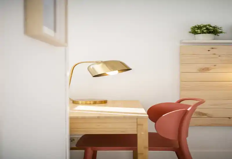 Rincón de salón luminoso y minimalista con escritorio de madera, lámpara dorada y silla roja moderna — un lugar acogedor para leer o trabajar.