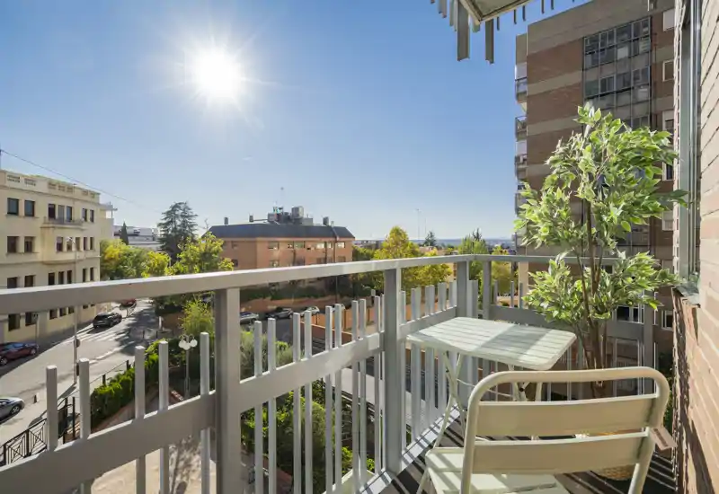 Balcón soleado con mesa y silla, agradable vista urbana y vegetación — ideal para tomar café por la mañana.