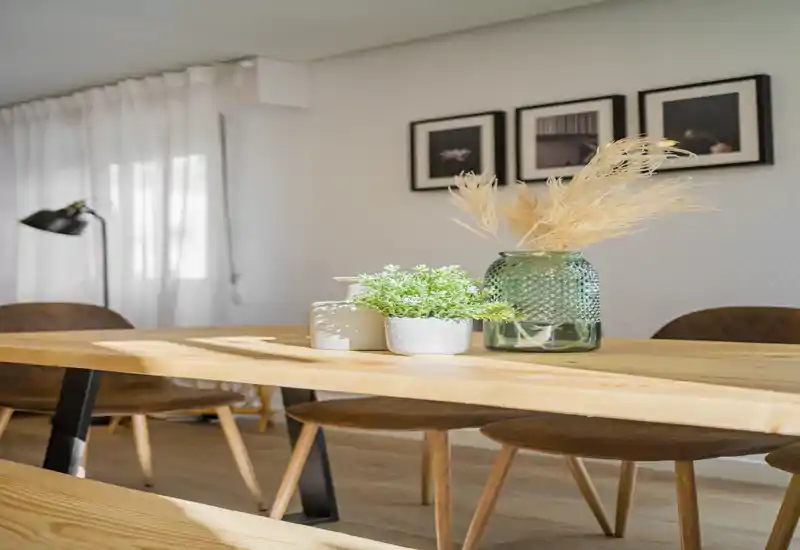 Zona de comedor estilosa con mesa de madera maciza, sillas cómodas y jarrones decorativos — luminosa, cálida y bien presentada para alquileres.