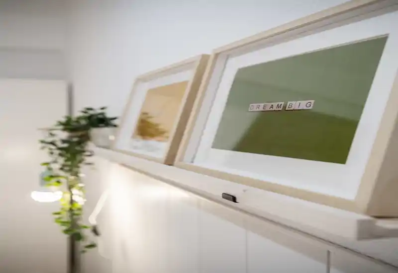 Close-up of decorative framed prints on a narrow shelf with a trailing plant and soft wall lighting; a detail shot of home decor rather than a specific room view.