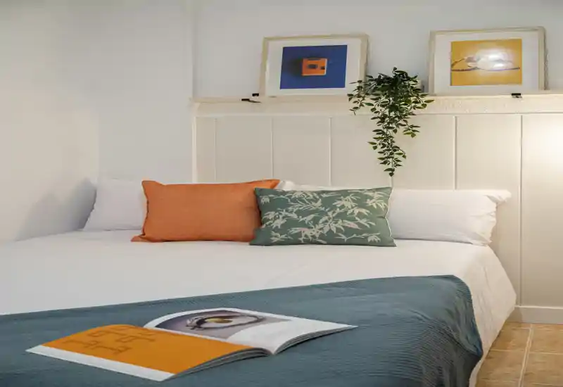 Bright, well-styled bedroom with a large bed, decorative cushions and a teal throw — ideal for comfortable short-term stays.