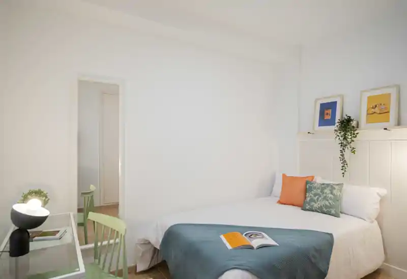 Bright, neatly styled bedroom with a double bed, decorative pillows, a teal throw and framed artwork for a cozy feel.