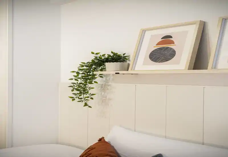 Bright, styled bedroom headboard shot with framed art and a trailing plant; clean linens and decorative cushions create a cozy, modern feel.