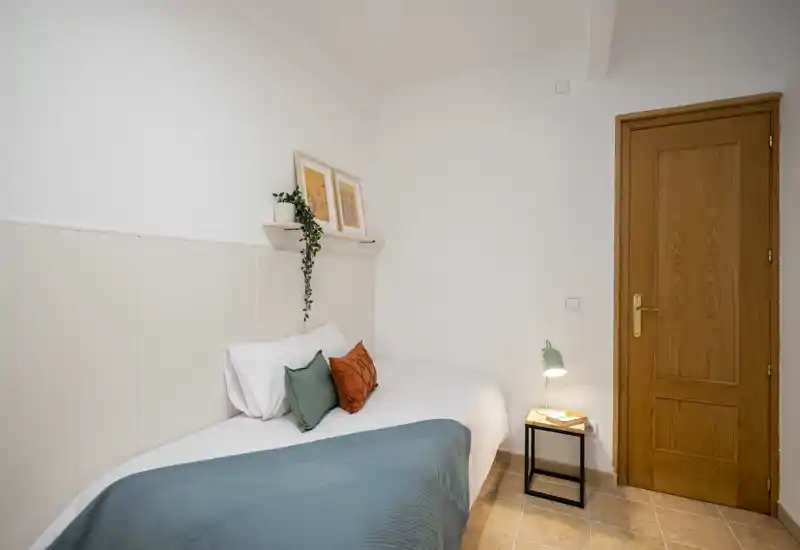 Habitación individual acogedora con cama bien hecha, cojines decorativos, mesita con lámpara — luminosa, sencilla y bien decorada para alquileres de corta estancia.