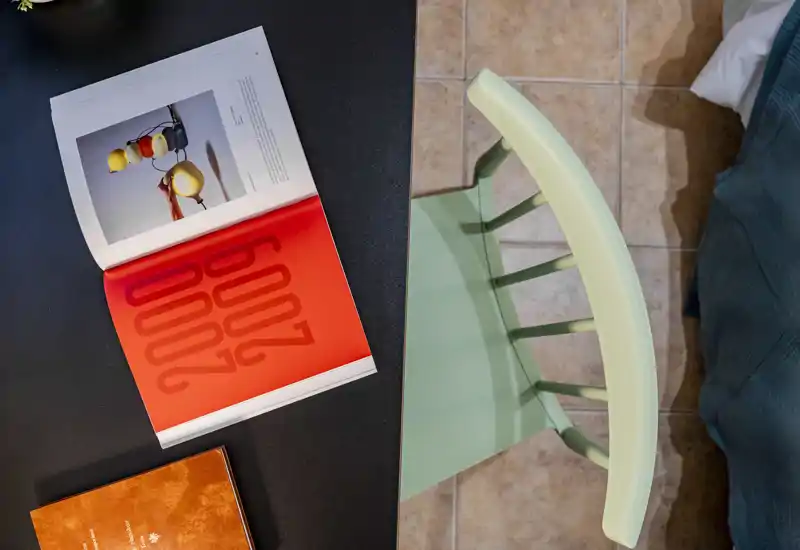 Vue plongeante d'un coin repas/travail avec une chaise, un sol carrelé et un livre ouvert sur une table sombre — un coin petit-déjeuner ou lecture chaleureux.