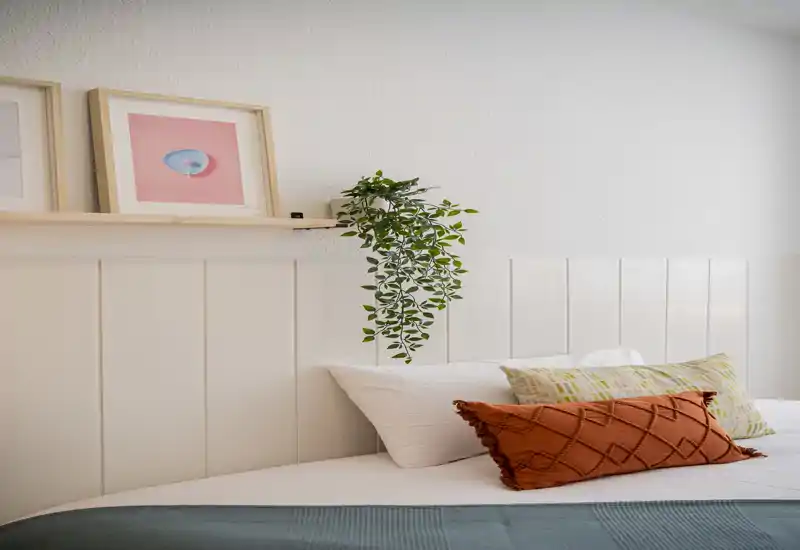 Angolo camera luminoso e curato con letto ben rifatto, cuscini decorativi e una pianta sospesa che crea un’atmosfera accogliente e moderna.