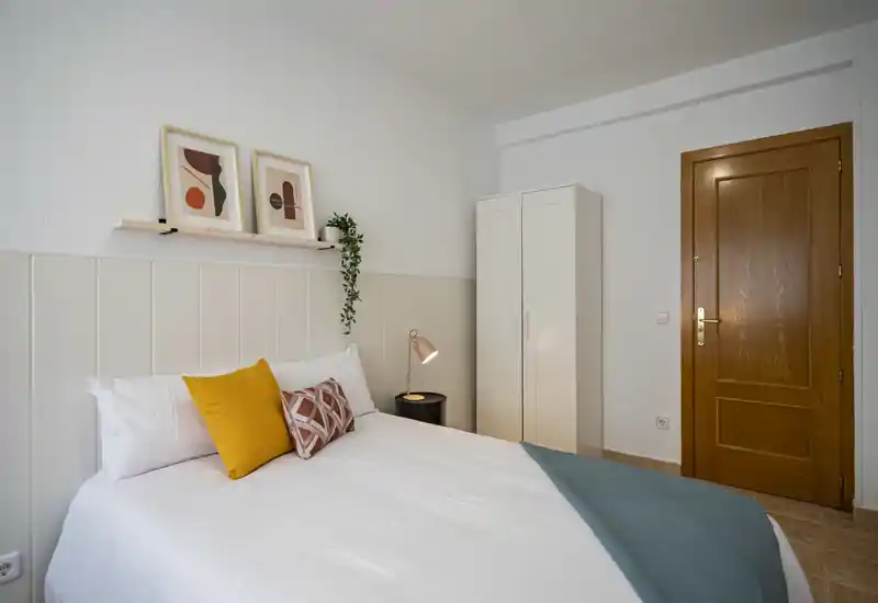 Camera da letto luminosa e curata con un letto matrimoniale ben rifatto, cuscini decorativi, lampada da comodino e armadio — accogliente e pronta per gli ospiti.