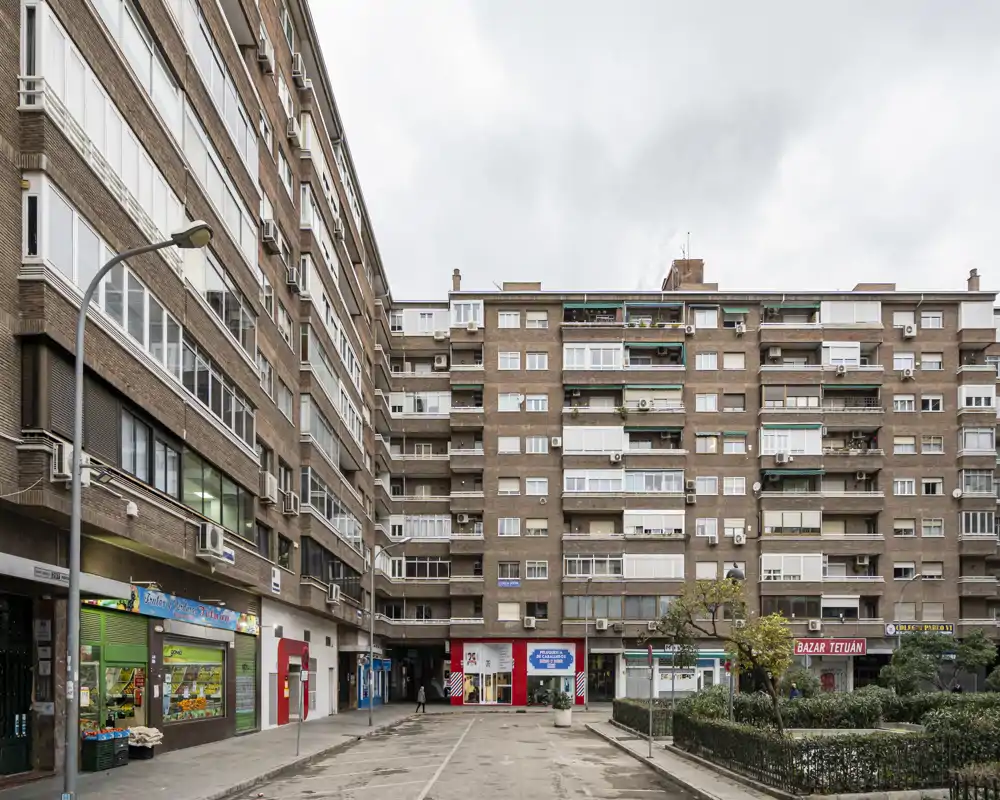 Exterior view of a residential courtyard and apartment block with ground-floor shops and balconies — clear, symmetric composition suitable for showing building facade and common outdoor space.