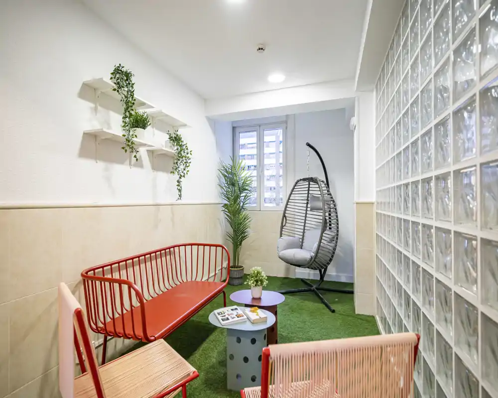 Bright, contemporary seating area with colorful chairs, a hanging rattan egg chair and greenery — ideal for relaxing or informal meetings.