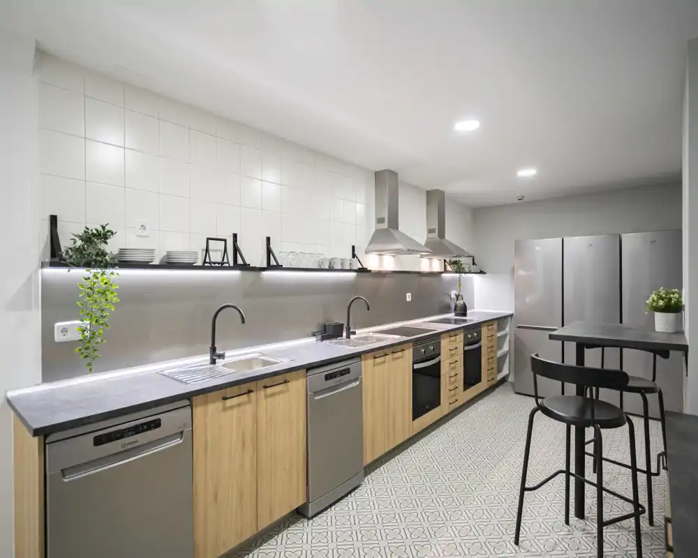 Modern shared kitchen with long counter, stainless appliances and wooden cabinets — bright, clean and well-equipped for group use.