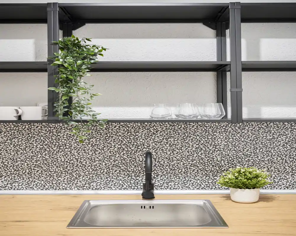 Modern kitchen sink area with a patterned backsplash, black faucet, open shelving and green plants that add a fresh decorative touch.