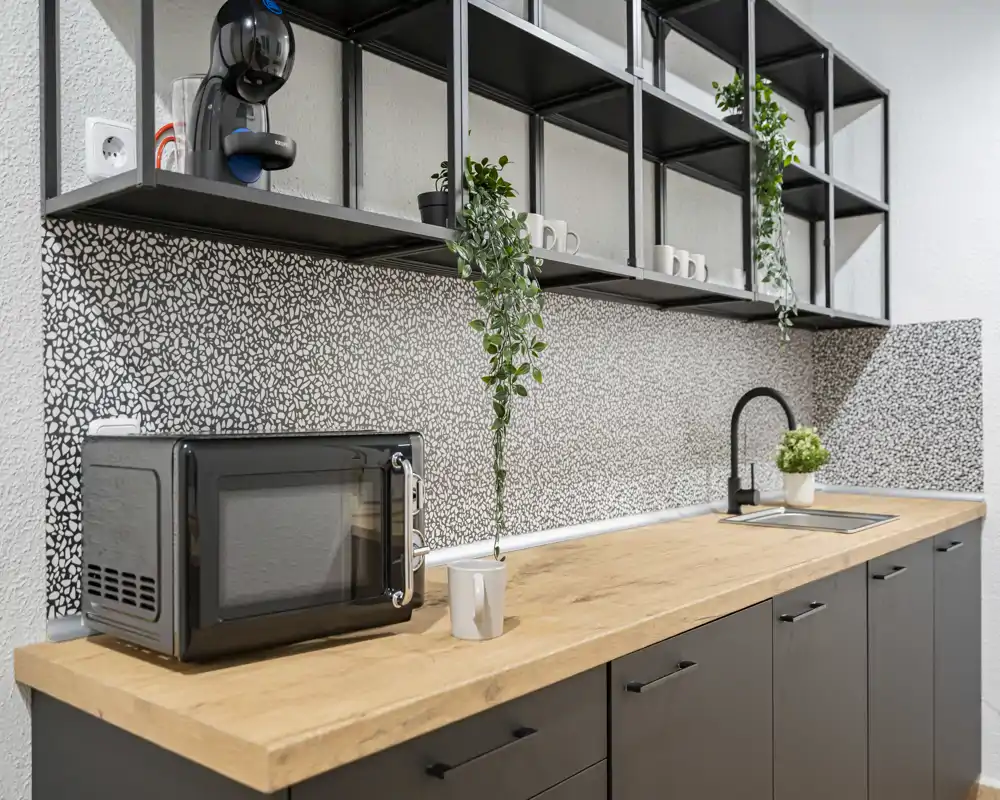 Modern compact kitchen with a wooden countertop, black cabinets, open shelving and a built-in sink; decorative plants and a microwave add practical charm.