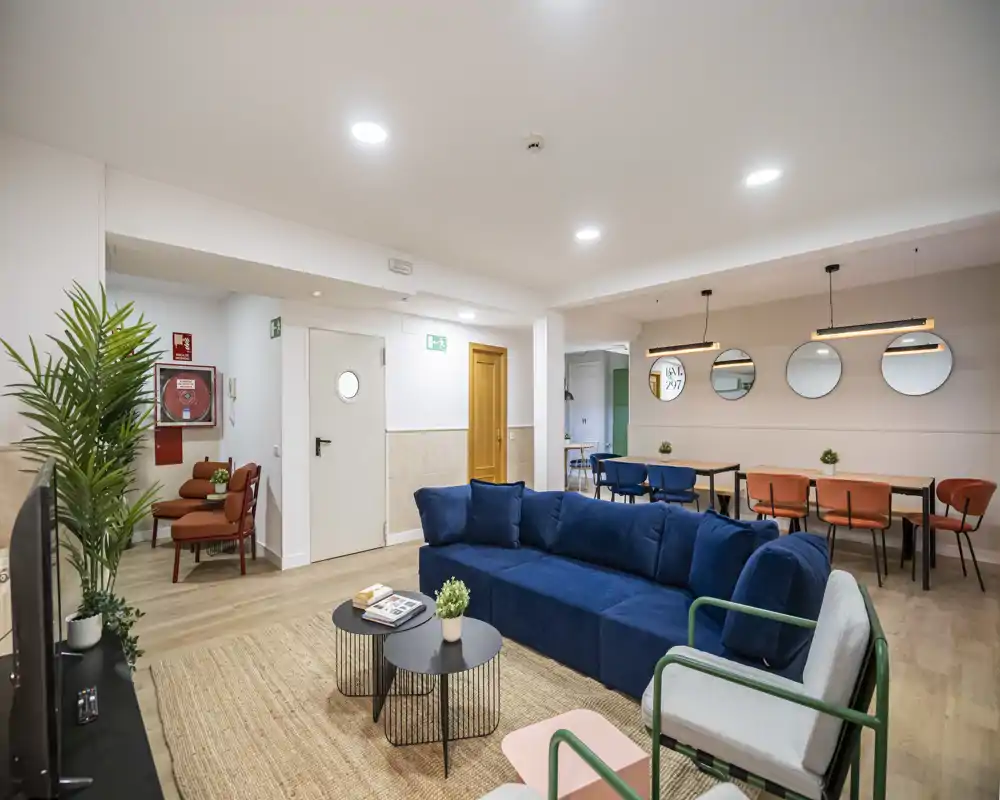 Spacious, modern living room with a deep blue sofa, natural-fiber rug and a dining area in the background — bright, stylish and ideal for socializing.