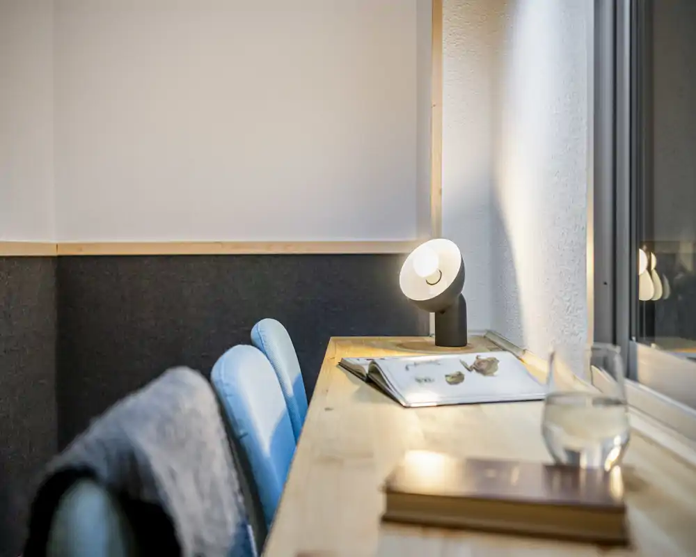 Cozy desk nook with two upholstered chairs, a warm desk lamp, books and a glass by the window — ideal for reading or light work.