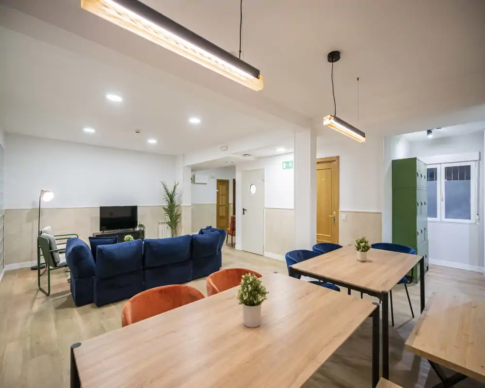Spacious, modern living area with comfortable blue sofas, communal wooden tables and warm pendant lighting — ideal for relaxed socializing or shared living.