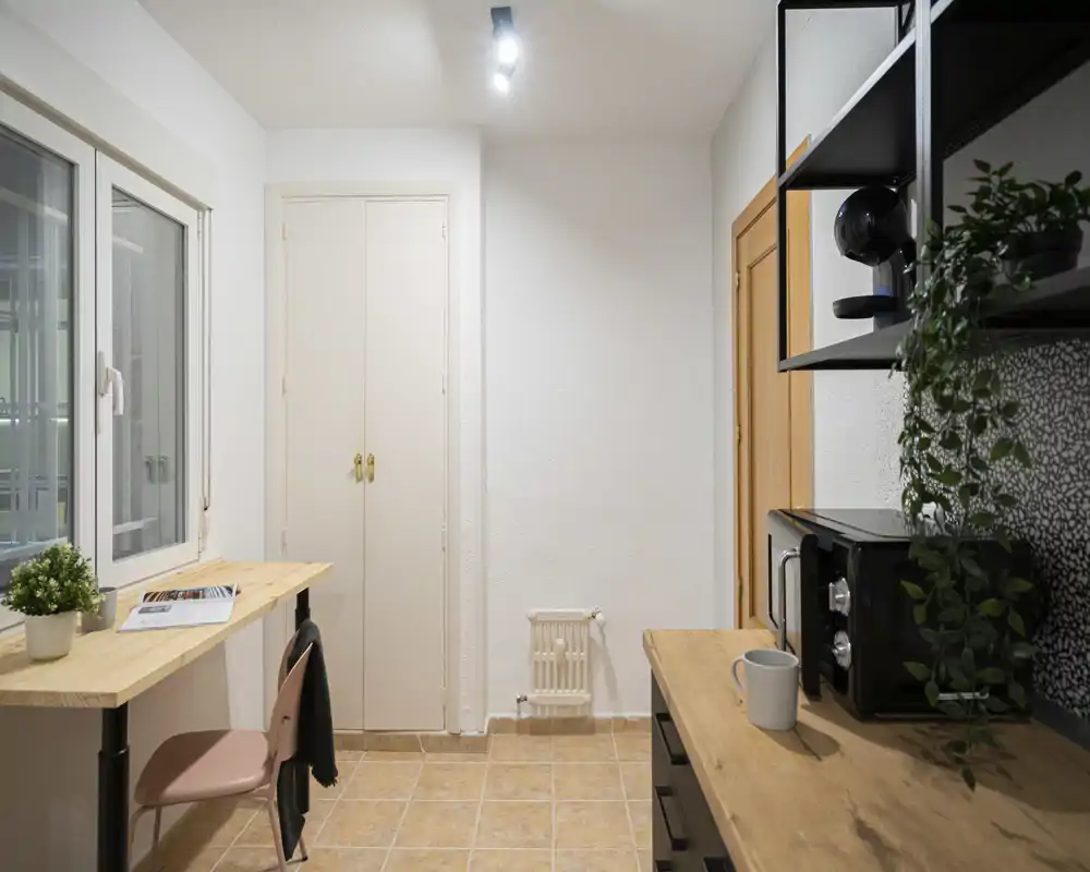 Compact kitchenette corner with wooden countertops, microwave, small work surface and a plant; bright, tidy and practical for short-stay rentals.