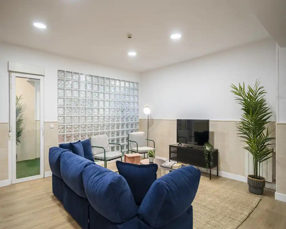 Bright, stylish living room with a deep blue sofa, paired armchairs, TV console and decorative plants — perfect for relaxing or entertaining.