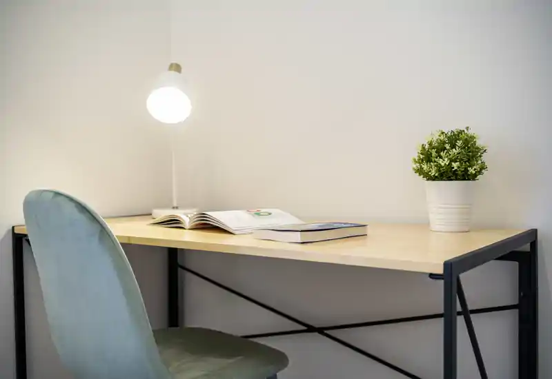 Espacio de trabajo compacto con escritorio de madera, silla verde tapizada, lámpara de mesa y pequeña planta en maceta: ideal como rincón de estudio en un alquiler.
