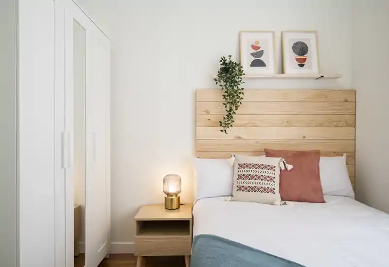 Camera da letto luminosa e moderna con testiera in legno, cuscini accoglienti, comodino e lampada — stile scandinavo ideale per affitti brevi.