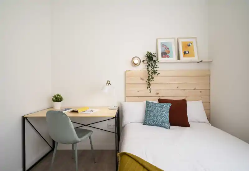 Chambre lumineuse et minimaliste avec tête de lit en bois, coussins décoratifs et un bureau bien rangé — idéale pour se détendre ou travailler.