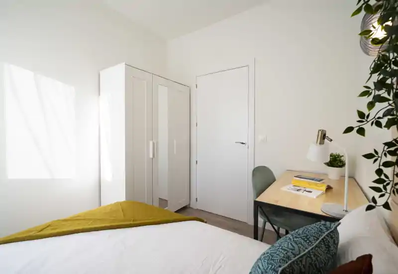 Dormitorio luminoso y minimalista con cama cómoda, armario y un pequeño escritorio — ideal para una persona. La luz natural y los textiles generan un ambiente tranquilo y acogedor.