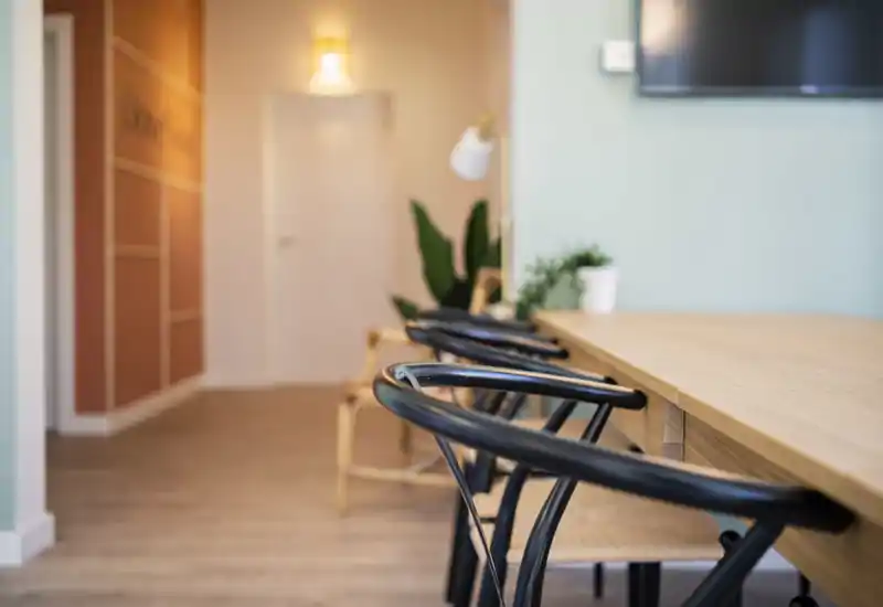 Primer plano de un comedor moderno con mesa de madera y sillas negras, iluminación suave y plantas que crean un ambiente cálido y acogedor.