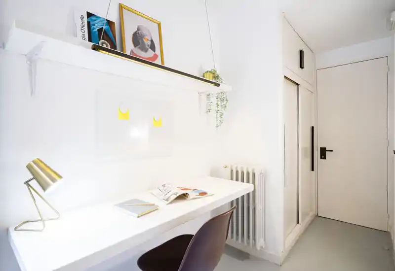 Entrada/pasillo luminosa y minimalista con un escritorio integrado, lámpara moderna y estantería: paredes blancas y un radiador compacto junto a la puerta.