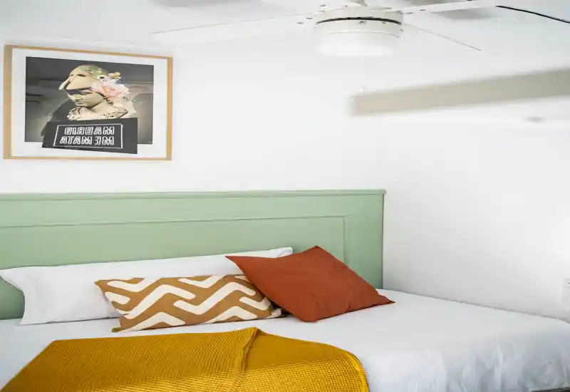 Dormitorio luminoso y estilizado con cabecero verde menta, cojines decorativos color óxido y una manta mostaza — imagen limpia y acogedora, ideal para anuncios.