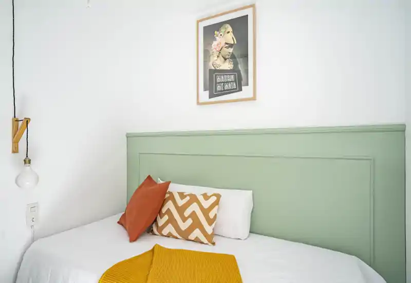 Dormitorio luminoso y con estilo con cabecero verde menta, cojines decorativos y una manta mostaza cálida, ideal para anuncios acogedores.