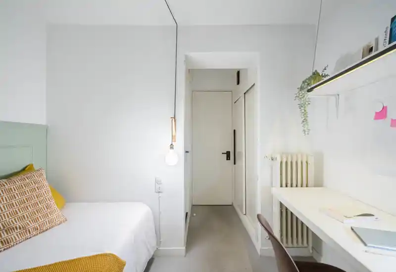 Bright, compact bedroom with a neatly made single bed, warm textiles and a functional desk area — ideal for a comfortable stay or work-from-home night.