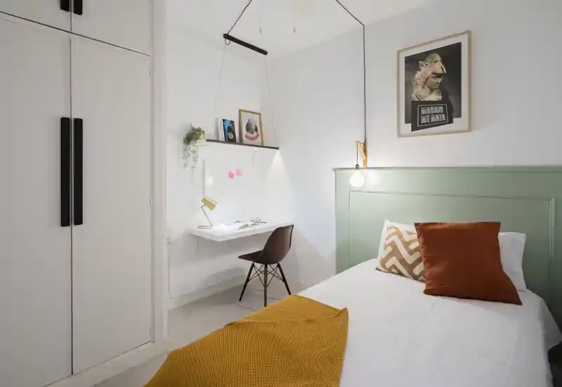 Chambre simple lumineuse et soignée avec tête de lit verte, textiles chaleureux et un coin bureau compact — idéale pour une location accueillante.