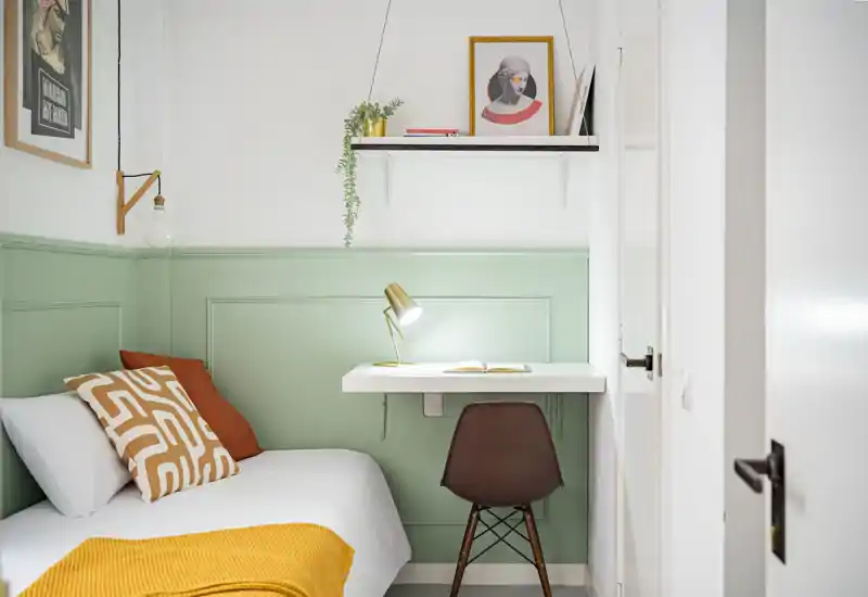 Bright, styled small bedroom with a single bed, decorative cushions and a compact study corner with a lamp — ideal for a cozy solo rental.